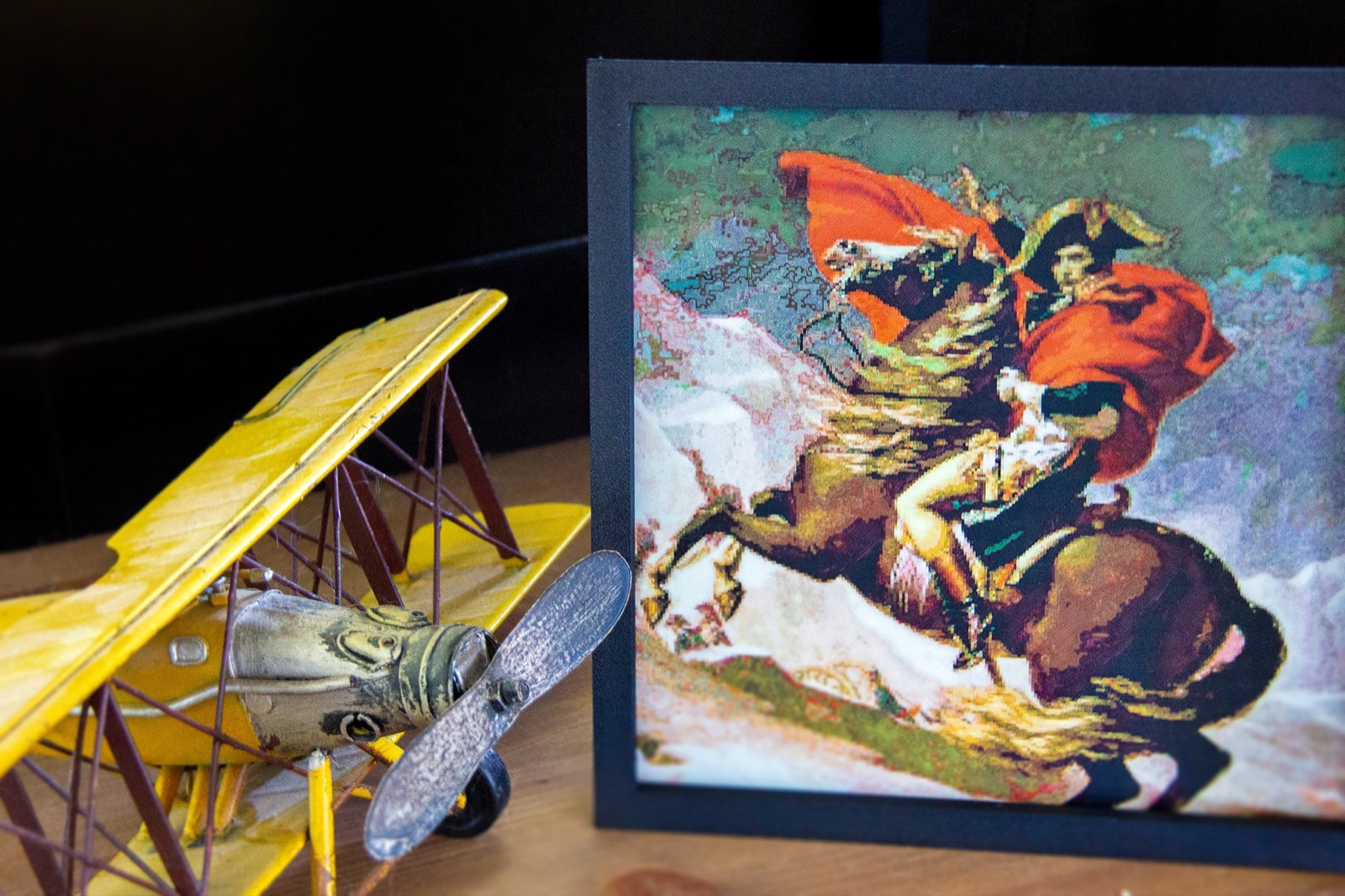 A framed Napoleon Crossing the Alps print beside a yellow model biplane