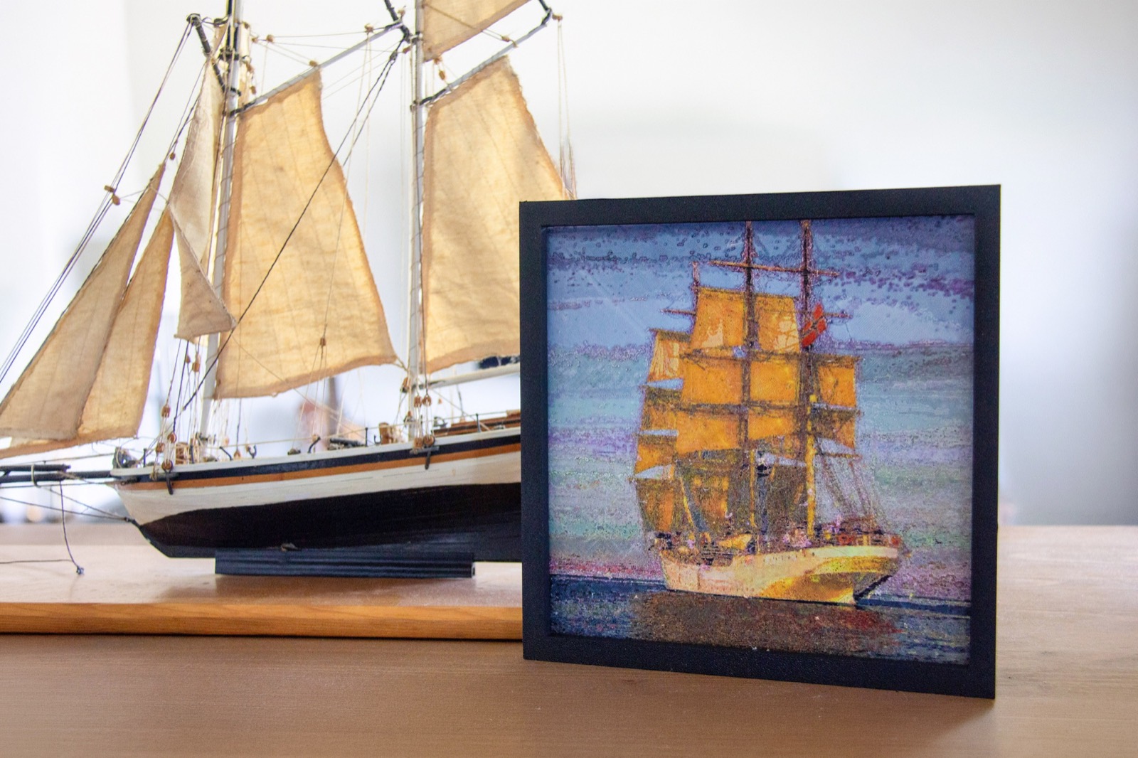 A framed print of a tall ship beside a model sailing ship on a shelf