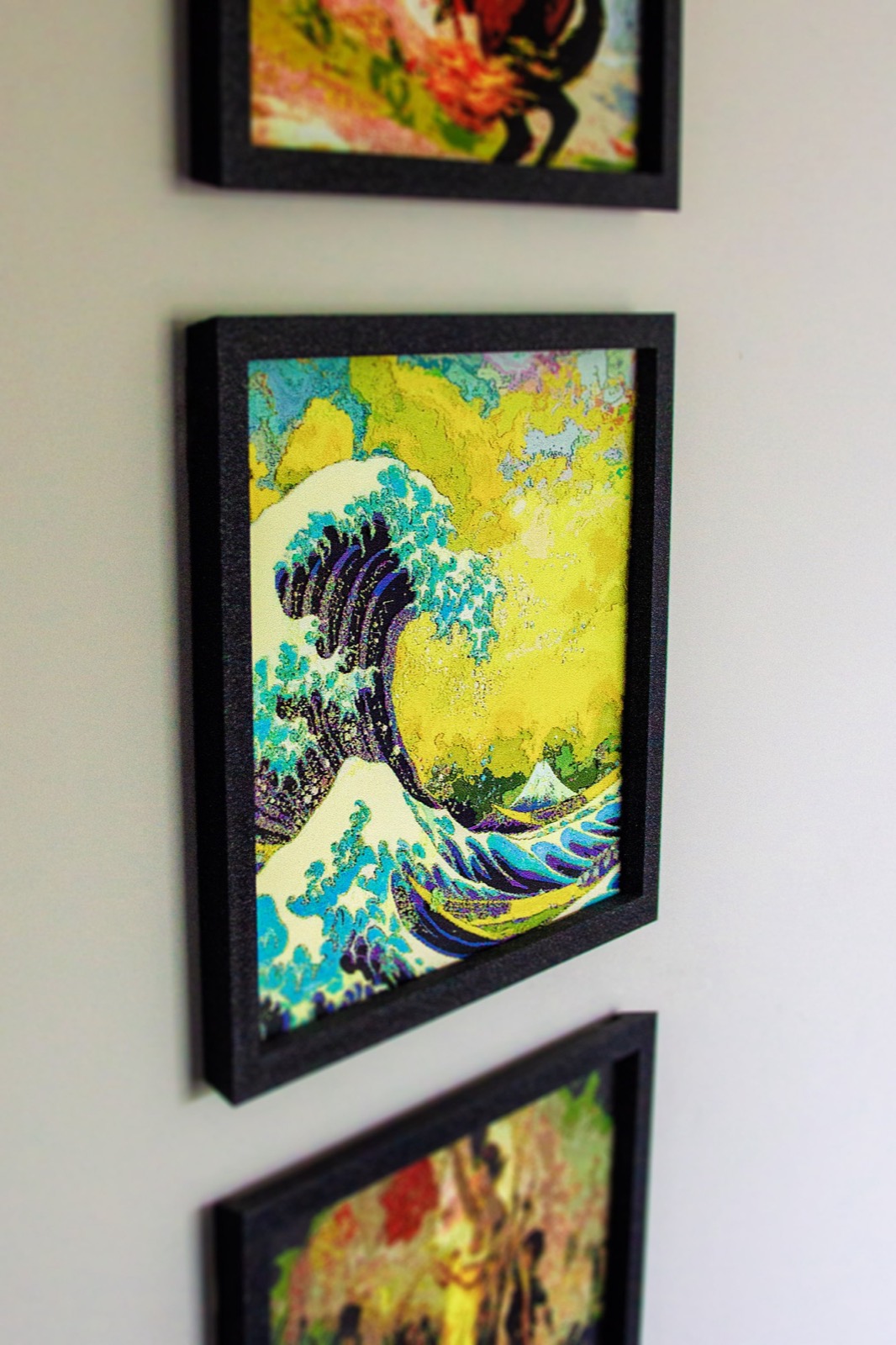 Three framed Polychrome prints hung in a column on a wall, The Great Wave in the middle