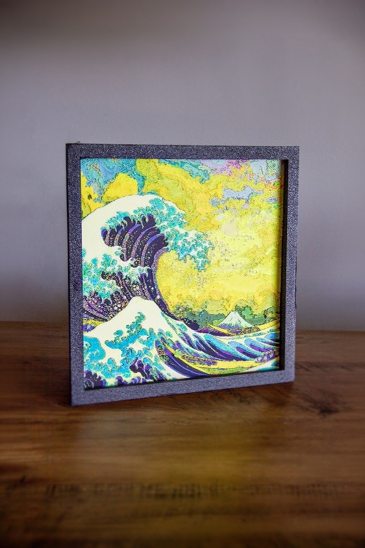 A framed relief print of The Great Wave on a wooden table
