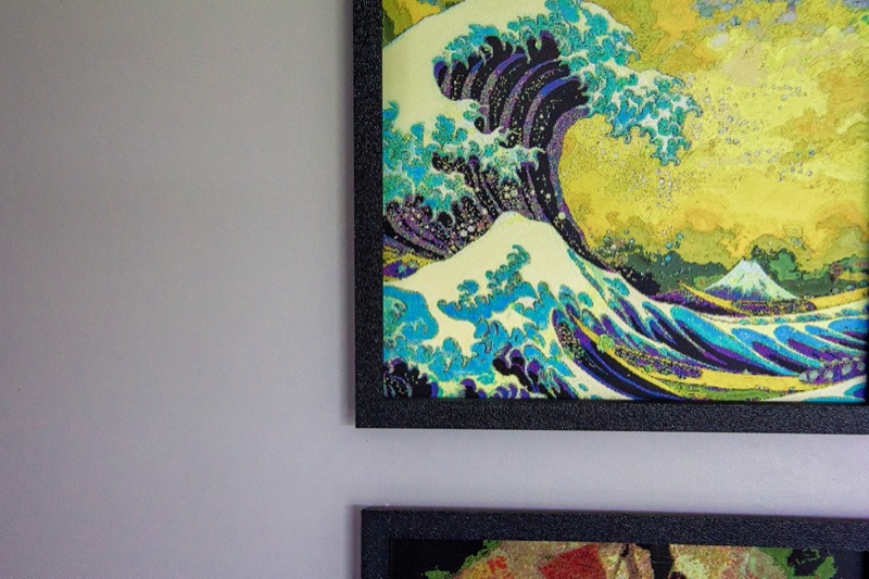 A framed Great Wave print on a wall, lit from the side